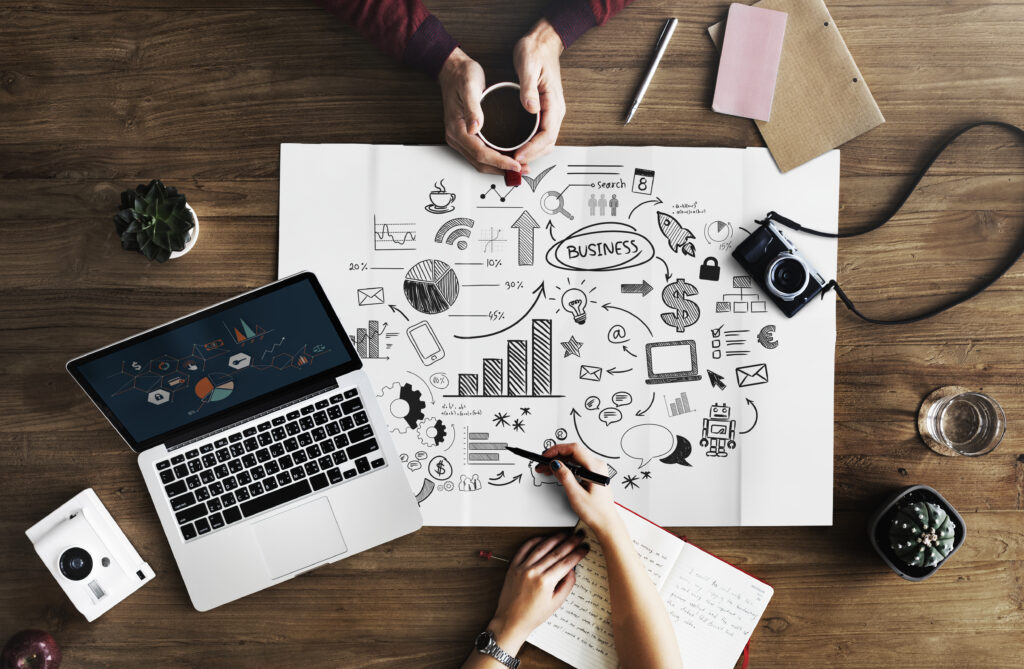 Un OBM et un entrepreneur réfléchissent autour d'un projet sur une table avec un ordinateur et cartographie de systèmes et indicateurs de performances. OBM Online Business Manager Directrice des opérations Operating Partner