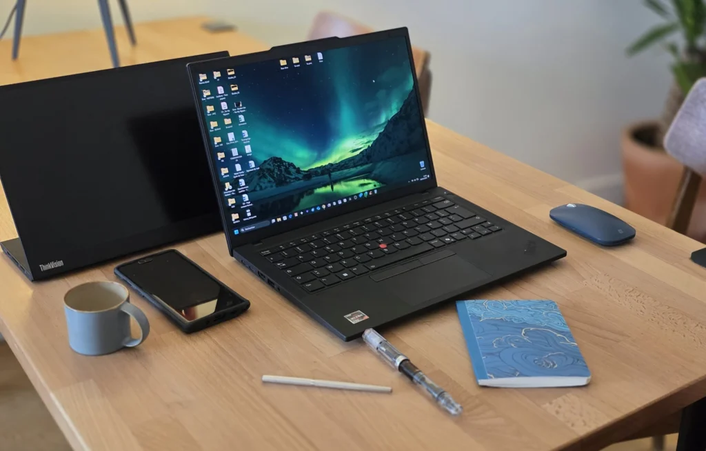 Présentation d'un bureau avec un ordinateur portable, un cahier, 2 stylos, une tasse de café et un écran portable d'ordinateur.